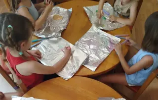 Cuatro niños pintando sobre papel de aluminio en la colonia artística de Rayuela